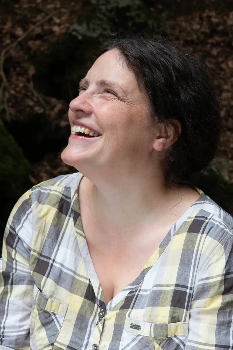 Anna Skryjová se smíchem zvedá hlavu, v pozadí tmavá skála